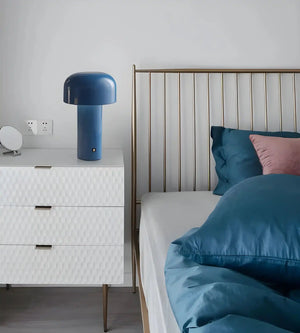 Modern bedroom featuring a metal-framed bed with blue bedding and a white dresser topped by a blue mushroom-shaped lamp.