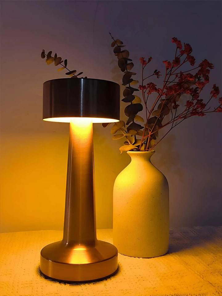 Modern table lamp with a cylindrical base and a wide, flat shade emitting warm light.