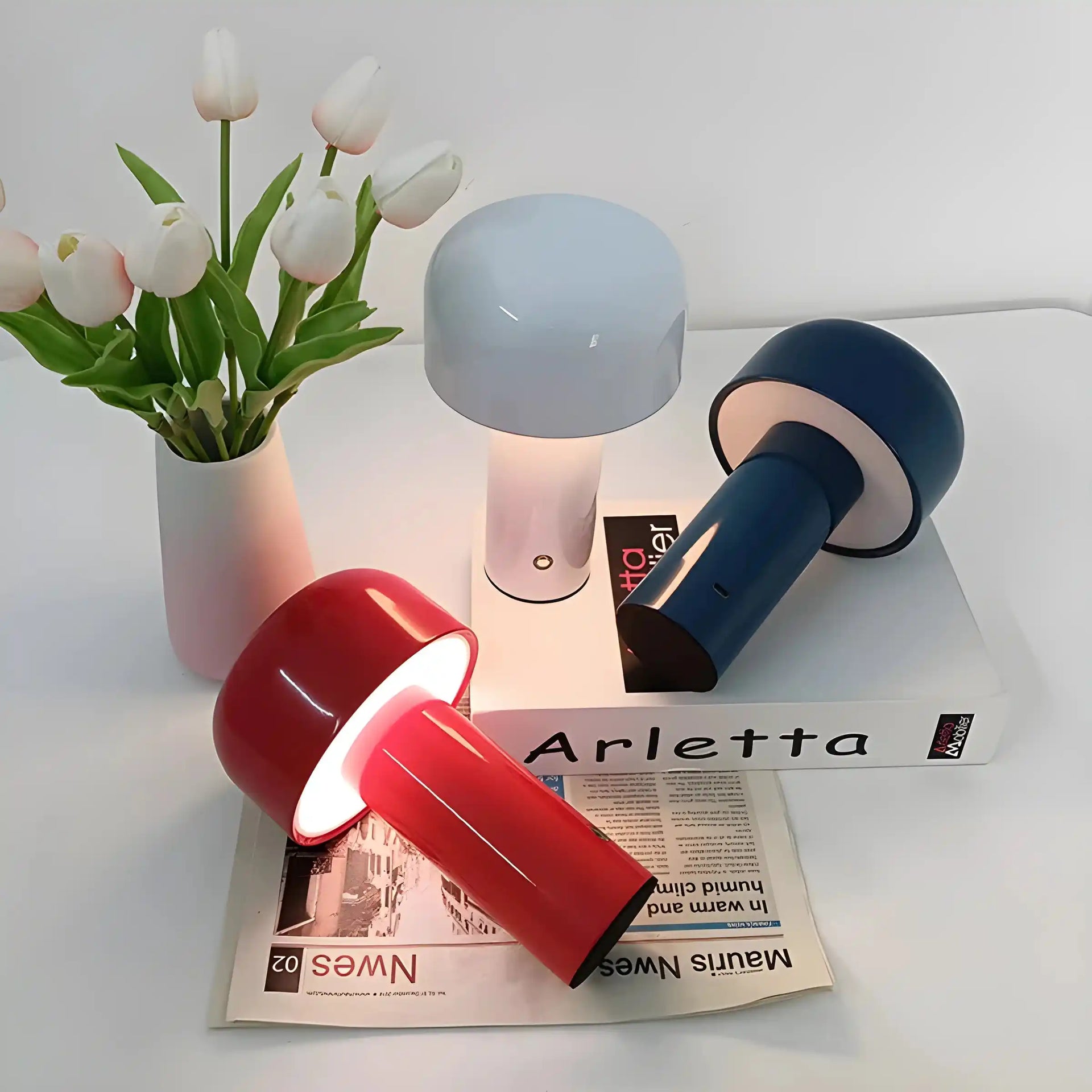 Collection of modern table lamps in various colors alongside a vase of white tulips.