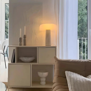 White modular storage unit with cubby spaces and doors, displaying decorative objects and a lit lamp on top.